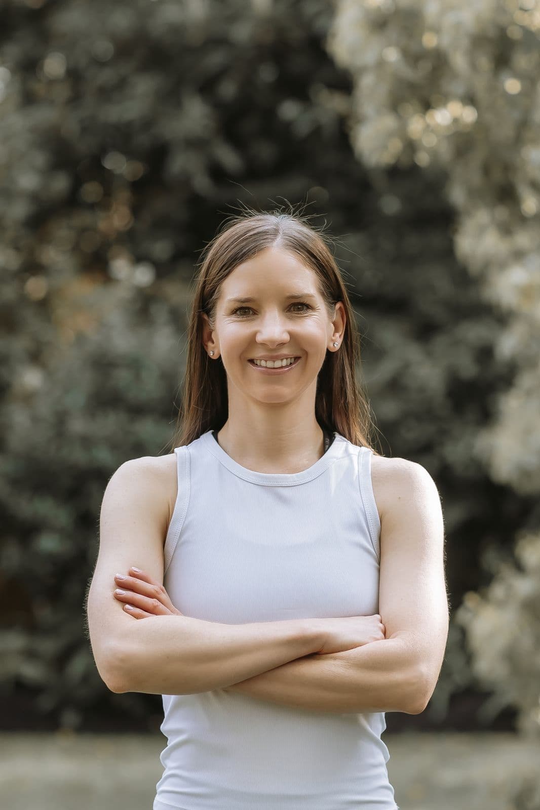 Siân Collins, Pilates teacher, smiling outdoors with arms folded against a leafy garden backdrop