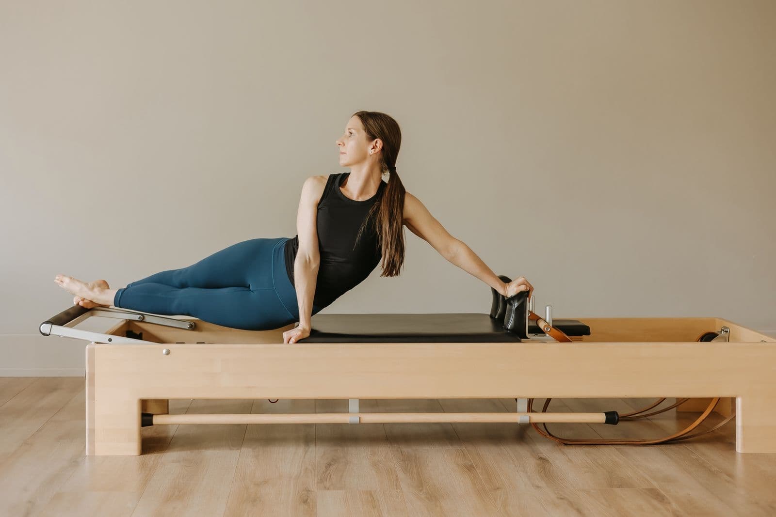 Siân in a long, lifted stretch on the reformer, hands on the footbar